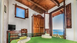 A bedroom with a bed, a wooden wardrobe, a desk with a television, and a view of the sea. - B&B La Torretta - Double Room with Sea View (Cersuta)