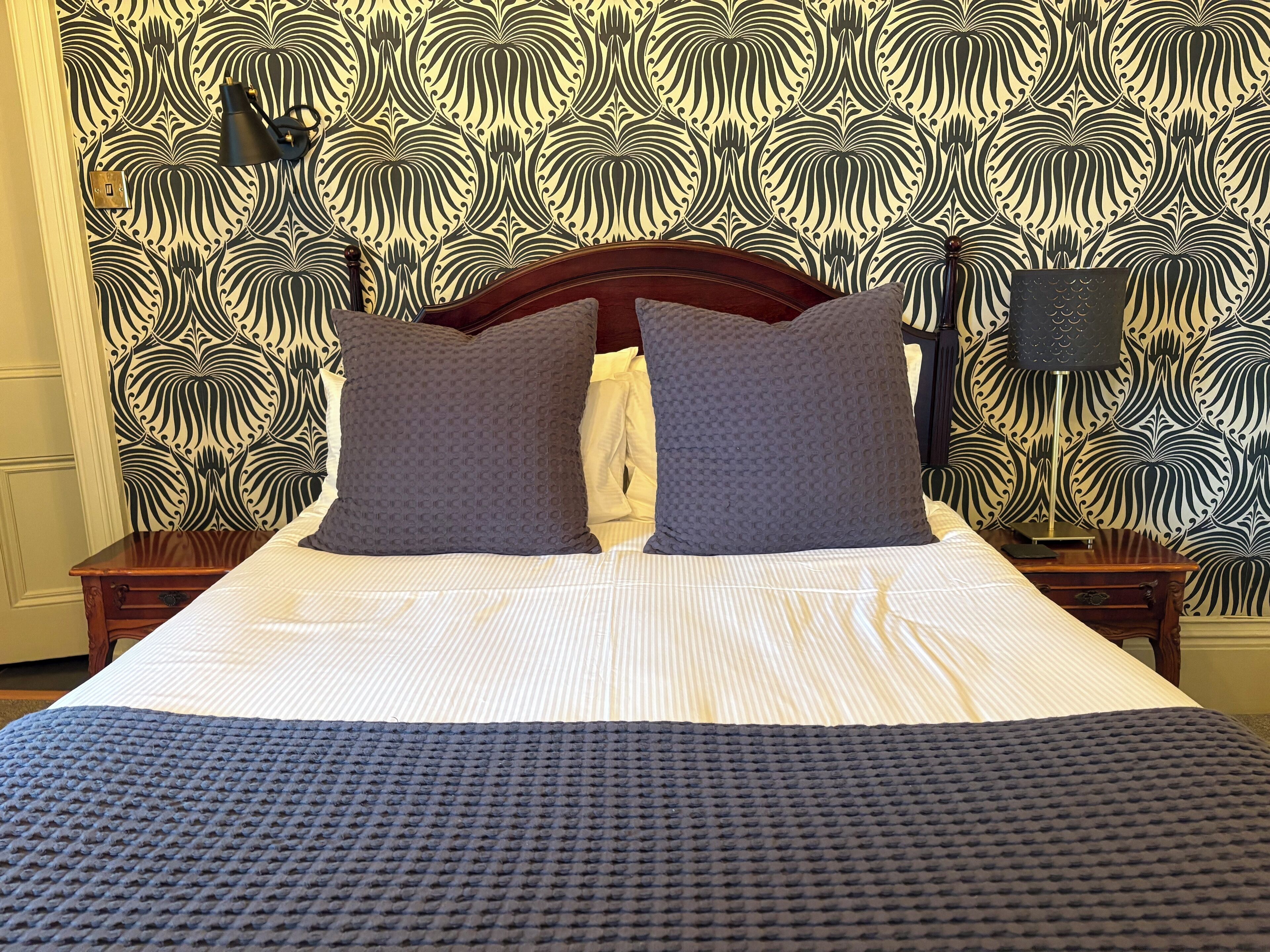 A neatly made bed with a white and blue striped bedspread, two gray pillows, and a wooden headboard.
