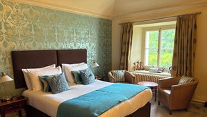Ein Schlafzimmer mit einem großen Bett, einem Sessel, einem kleinen Tisch und einem Fenster mit Vorhängen.