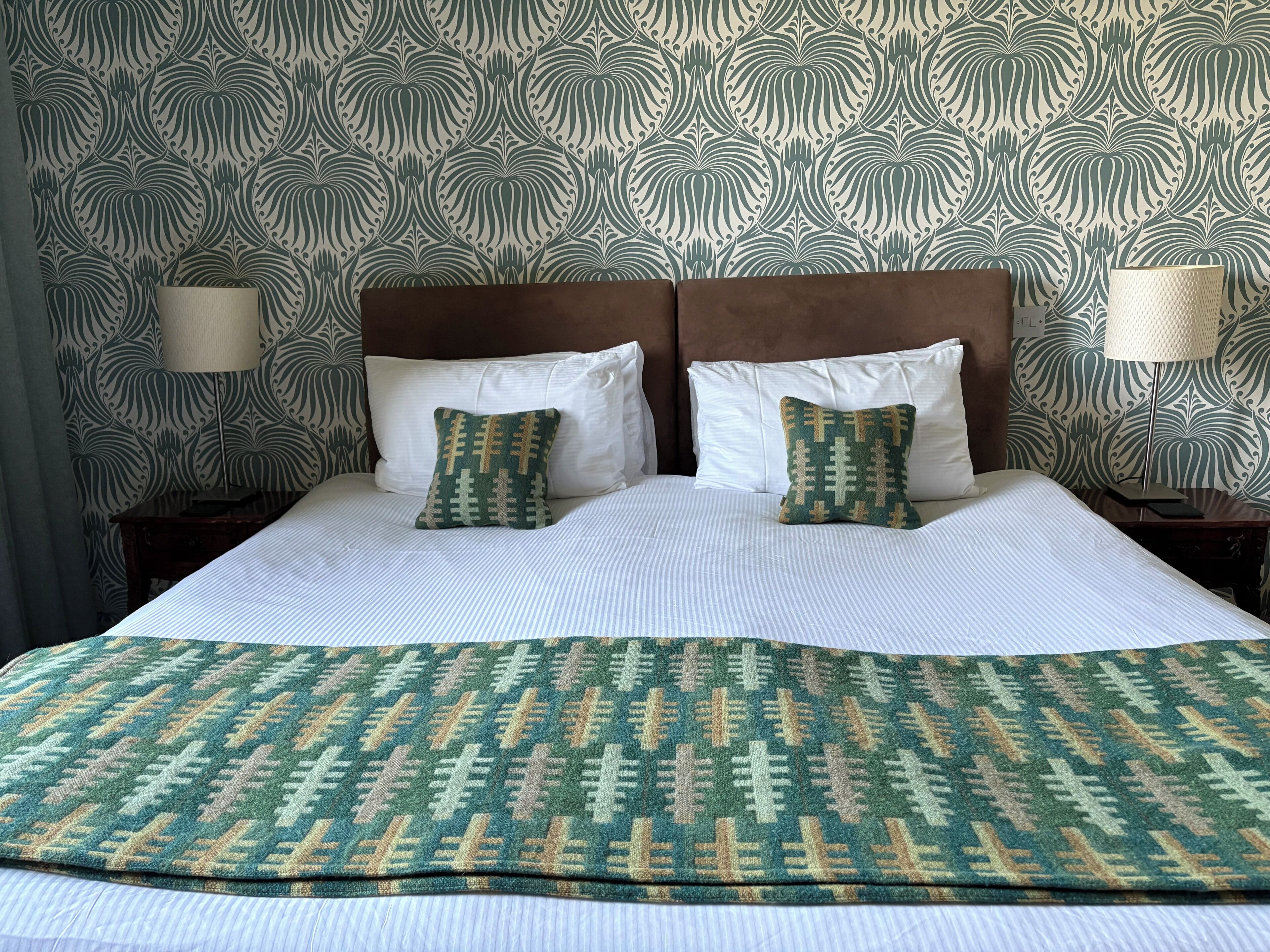 Una cama bien hecha con una colcha estampada y dos almohadas, un cabecero de madera y dos lámparas de noche.