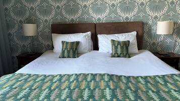 Una cama bien hecha con una colcha estampada y dos almohadas, un cabecero de madera y dos lámparas de noche.