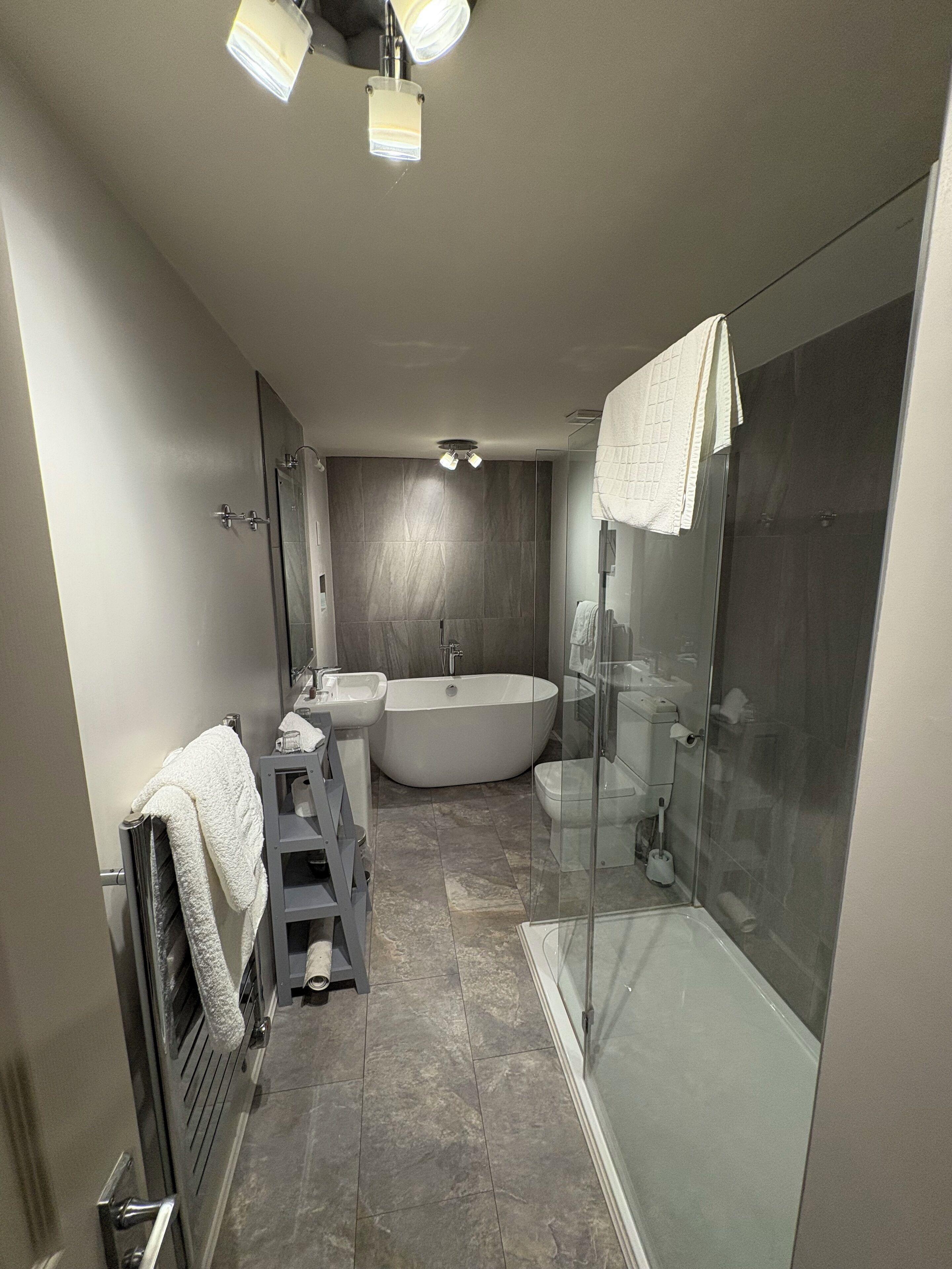 Ein modernes Badezimmer mit einer freistehenden Badewanne, einer in Glas abgeschirmten Dusche und einem Waschtisch mit Waschbecken und Spiegel.