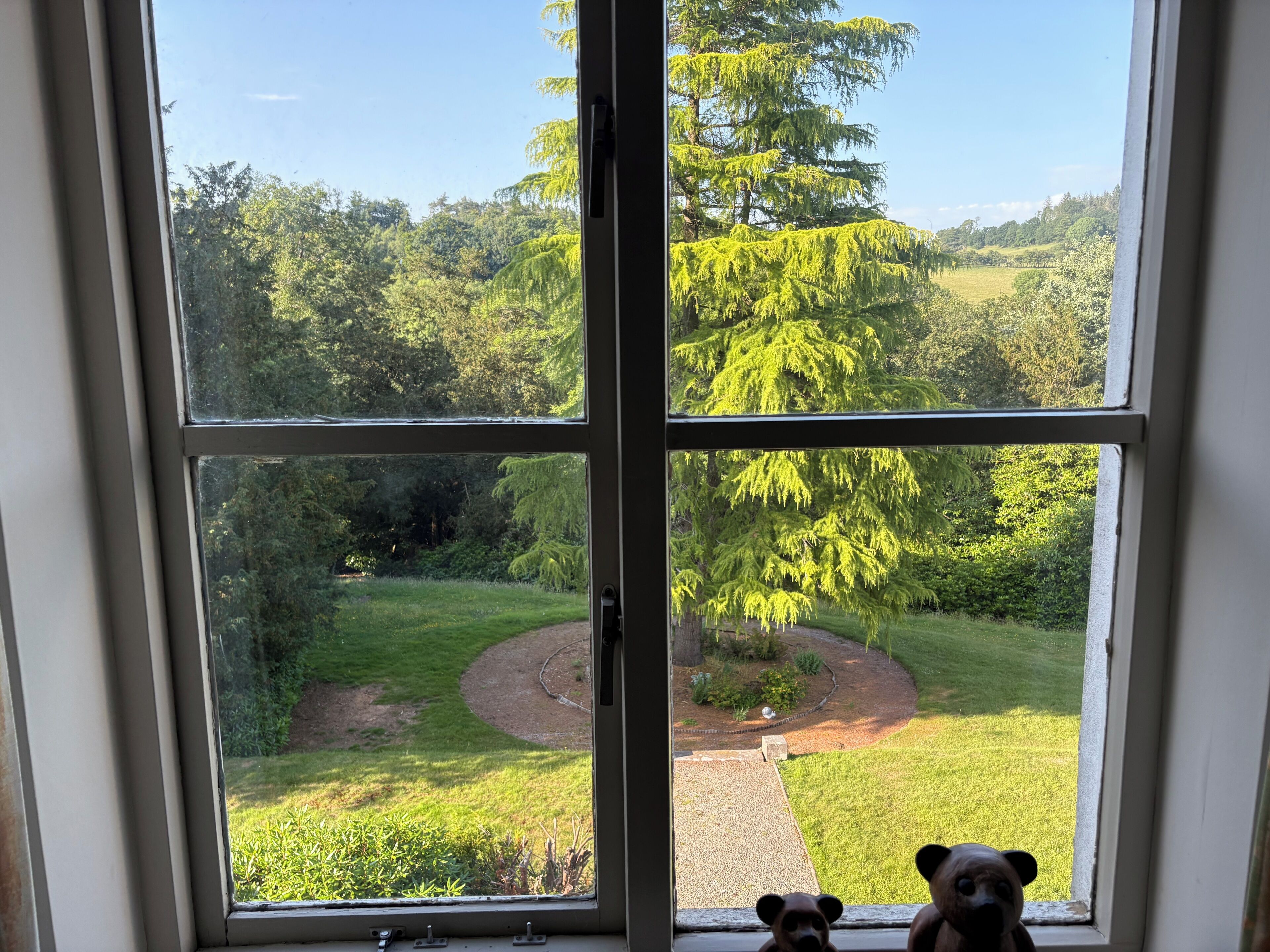 Una ventana con vistas a un jardín, un sendero y una pequeña figura de un oso en el alféizar.