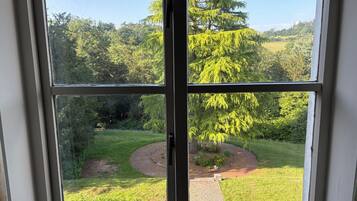 A window with a view of a garden, a pathway, and a small bear figurine on the windowsill.