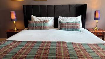 Una cama bien hecha con una colcha escocesa, dos almohadas a juego y dos lámparas de noche sobre mesitas de madera.