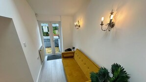 A hallway with a yellow sofa, a potted plant, and wall-mounted lighting fixtures. - Batheaston Terrace (Batheaston)