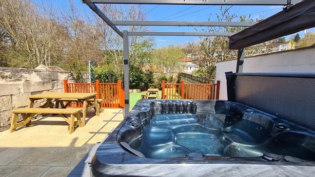 A hot tub under a pergola with a wooden table and chairs nearby. - Batheaston Terrace (Batheaston)