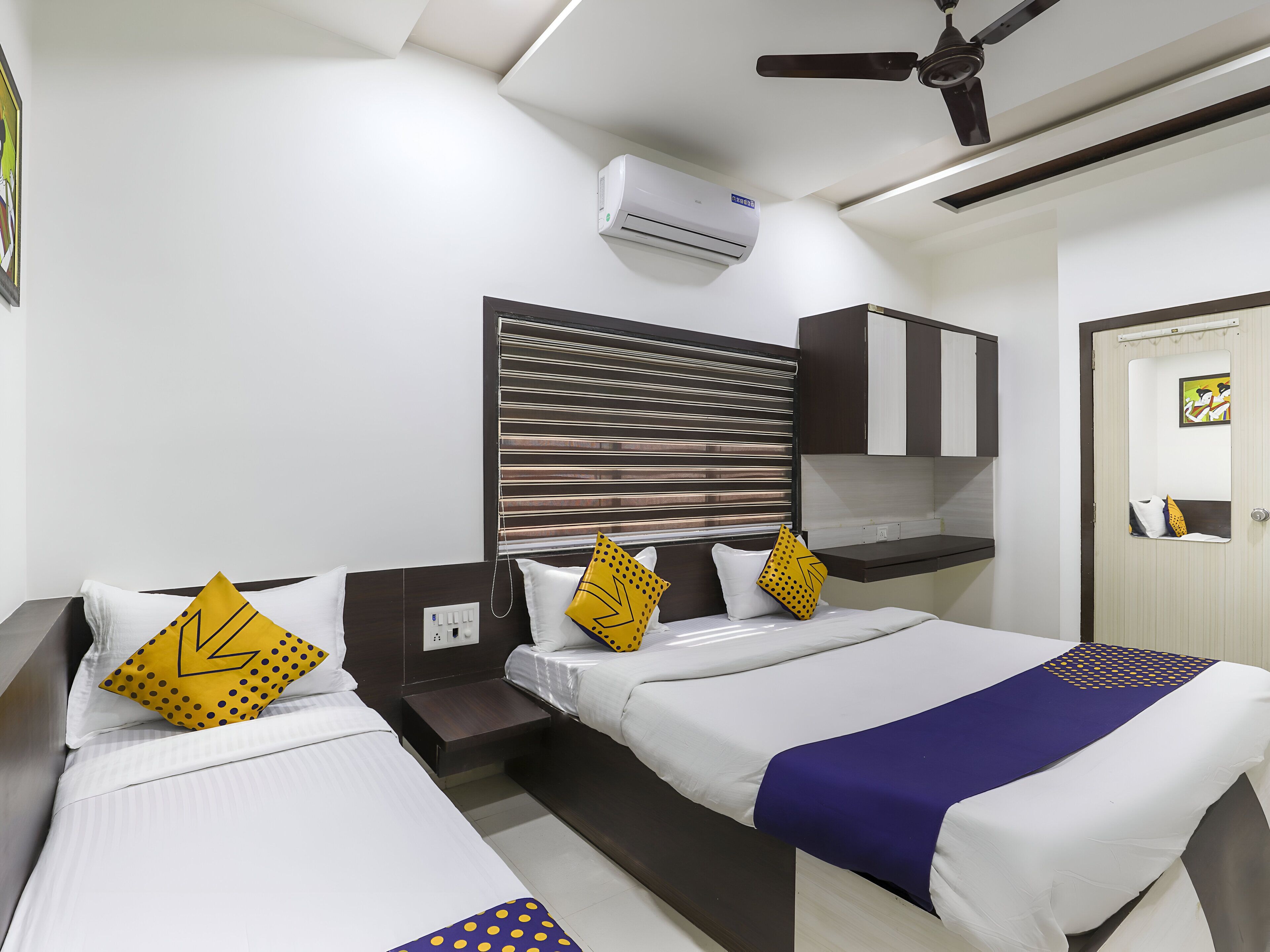 A hotel room with two single beds, a ceiling fan, an air conditioning unit, and a door with a mirror.