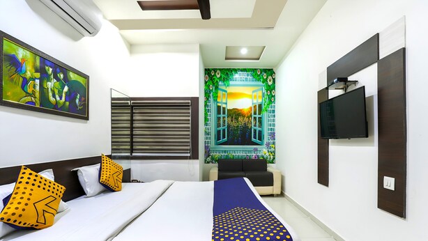 A hotel room with a bed, a TV, and a mural with an open window. - Hotel Atithi - Opposite Shreeji Hospital (Rajkot)