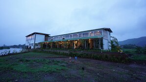 Un edificio de dos plantas con techo plano y ventanas amplias, ubicado cerca de una masa de agua.