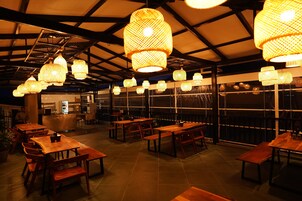Un restaurante con mesas y bancos de madera, faroles de papel colgantes y vistas amplias por las ventanas.