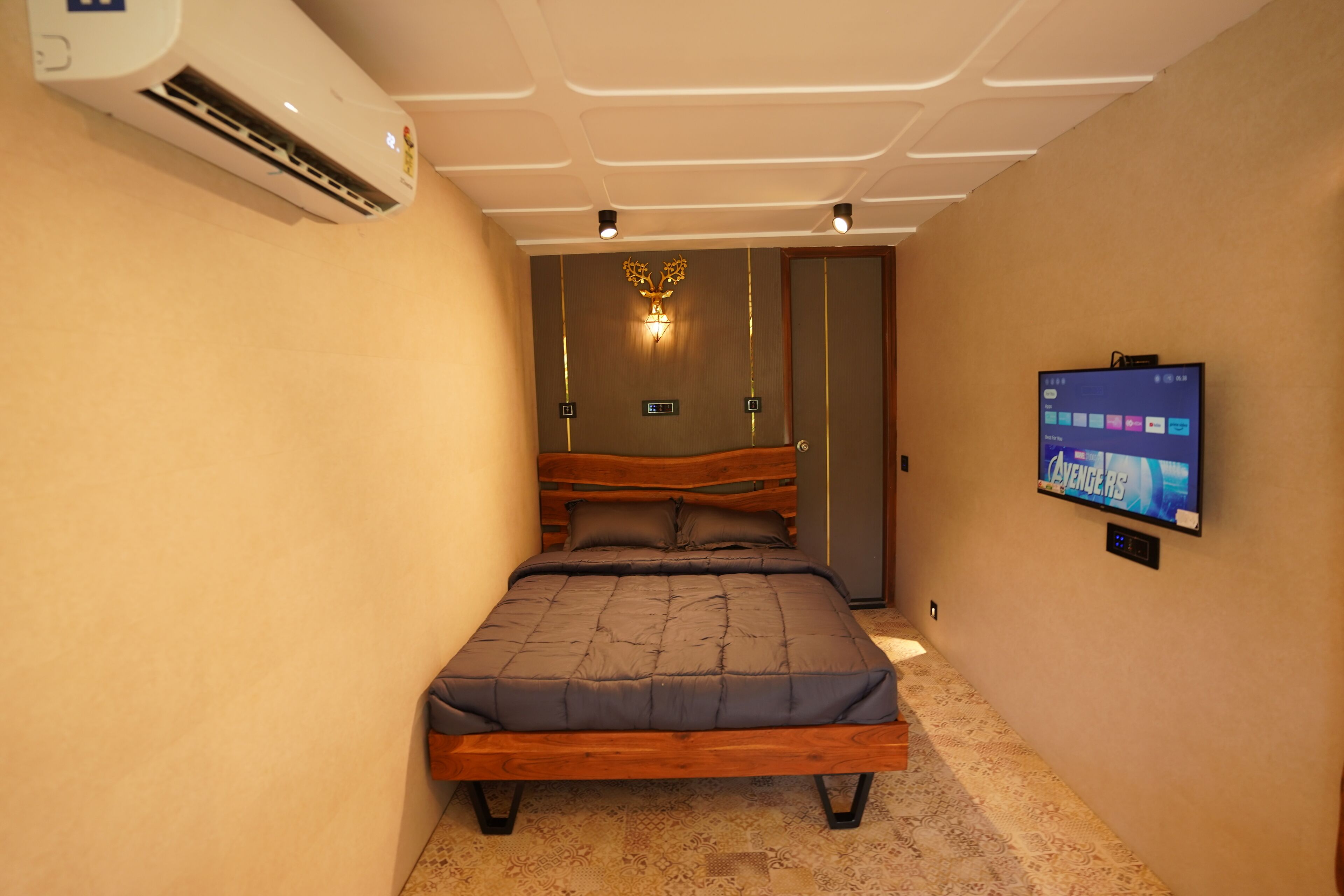 Un dormitorio con cama, aire acondicionado, televisor montado en la pared y alfombra estampada.
