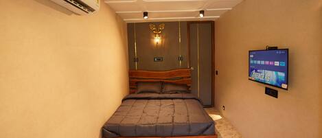 Un dormitorio con cama, aire acondicionado, televisor montado en la pared y alfombra estampada.