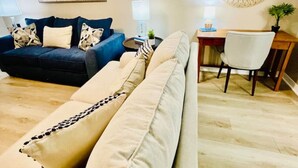 Ein Wohnzimmer mit einer Couch, einem Sessel, einem Schreibtisch und einem runden Spiegel an der Wand.