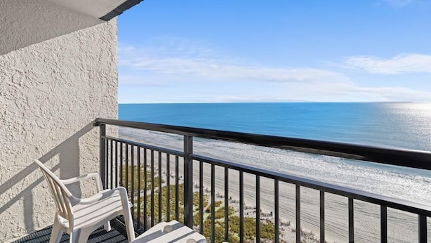 A balcony with a view of the ocean, a white chair, and a small table. - Roomy Oceanfront Ste Includes Breakfast 15th Flr (Myrtle Beach)