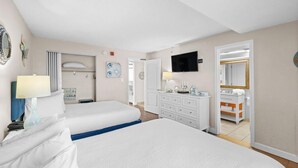 A hotel room with two beds, a TV, a bathroom with a mirror, and a dresser.