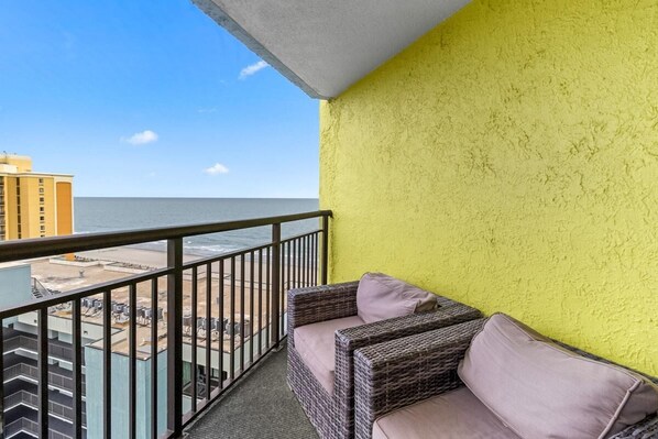 A balcony with wicker furniture and a yellow wall, overlooking a beach and ocean. - Ocean View Retreat: Includes Breakfast 14th Flr (Myrtle Beach)