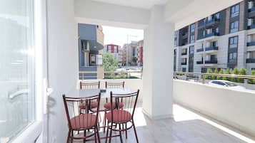 Un balcón con una mesa y sillas para comer, con vista a una calle con coches y edificios.