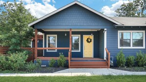 A two-story house with a front porch, a yellow door, and a wreath on the door.