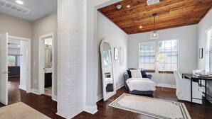 A spacious room with a wooden ceiling, a large mirror, a bed, a desk, and a chair.