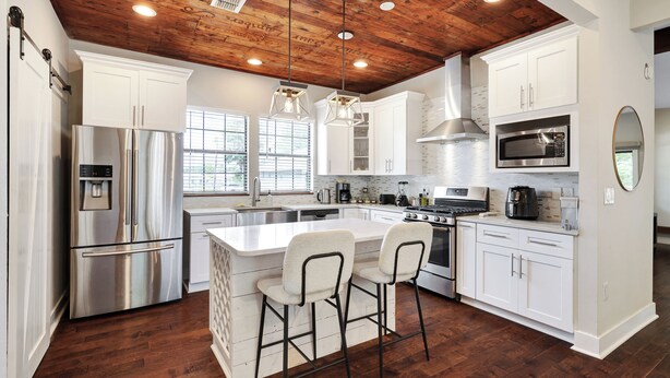 A modern kitchen with white cabinetry, stainless steel appliances, a wooden ceiling, and a central island with bar stools.