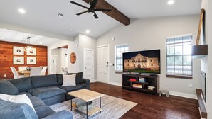 A living room with a sectional sofa, a wooden accent wall, a ceiling fan, a TV, and a window.