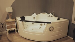 A corner room with a large freestanding bathtub, a small bedside table with a lamp, and a wall-mounted mirror. - DORIAN GRAY LUXURY SUITE (Trieste)