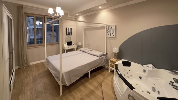 A bedroom with a four-poster bed, a bedside table with a lamp, a large window, and a jacuzzi tub. - DORIAN GRAY LUXURY SUITE (Trieste)