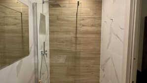 A modern bathroom with a large mirror, a sink, a shower, and a wooden accent wall. - DORIAN GRAY LUXURY SUITE (Trieste)