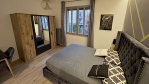 A bedroom with a bed, a wardrobe, a chair, a window, and a pendant light. - DORIAN GRAY LUXURY SUITE (Trieste)