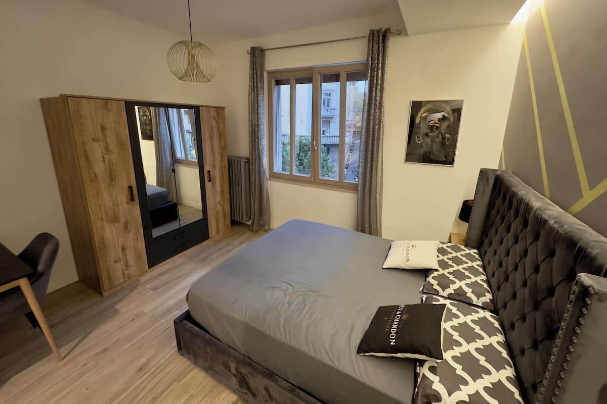 Un dormitorio con cama, armario, silla, ventana y lámpara colgante.