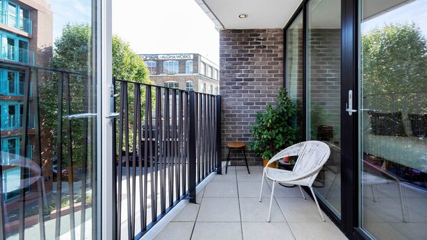 A balcony with a glass door, a white wicker chair, and a small table. - Boho-Chic Escape, by Veeve (London)