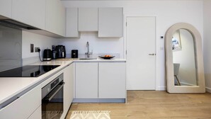 A modern kitchen with white cabinetry, a black induction cooktop, and a built-in oven. - Boho-Chic Escape, by Veeve (London)