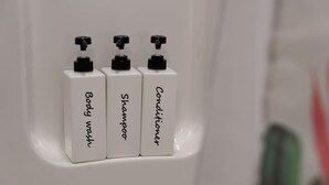 Trois flacons blancs étiquetés « gel douche », « shampoing » et « après-shampoing » sont posés dans une salle de bain.