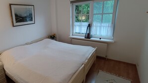 Un dormitorio con cama, mesita de noche, lámpara, ventana con cortinas y radiador.