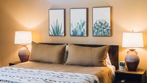 A neatly made bed with a patterned bedspread, two bedside lamps, and three framed botanical prints on the wall. - Hidden Gold House | Luxury Joshua Tree Retreat (Yucca Valley)