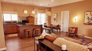 A modern kitchen with a central island, wooden bar stools, a dining area with a table and chairs, and a cozy seating area with a sofa and ottoman. - Hidden Gold House | Luxury Joshua Tree Retreat (Yucca Valley)