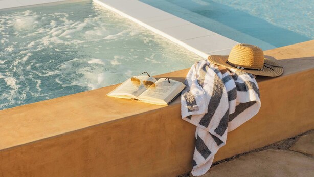 A poolside area with a towel, a hat, and an open book. - Hidden Gold House | Luxury Joshua Tree Retreat (Yucca Valley)