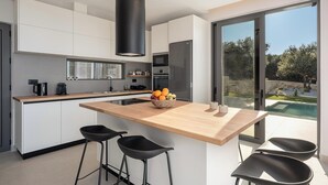 A modern kitchen with a central island, bar stools, and a view of the outdoors. - Villa Zefyros With Sea View (Platanias)