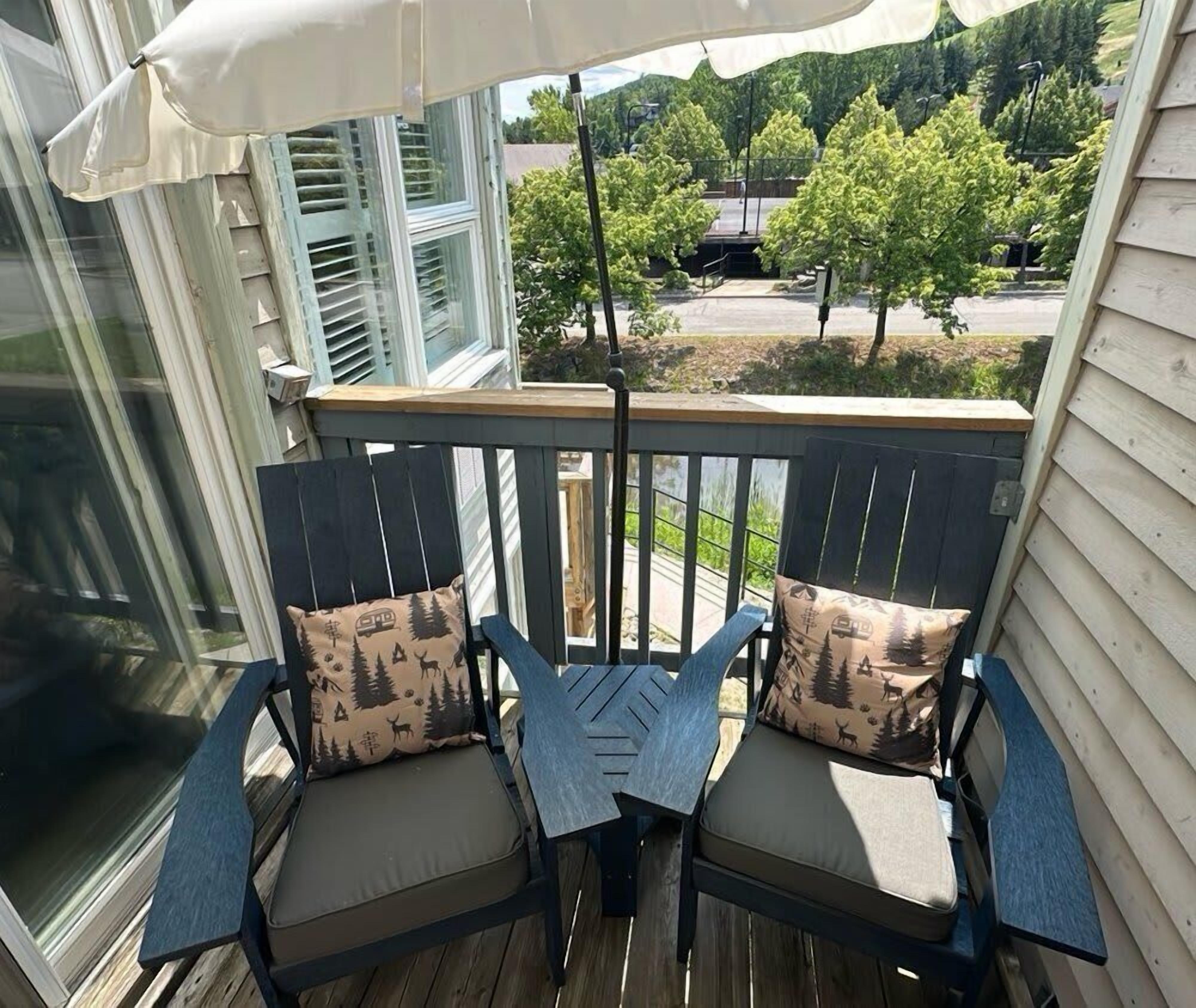 En träaltan med två stolar och ett bord, med utsikt över ett bostadsområde med träd och en väg.