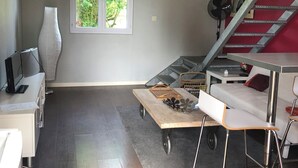 Ein modernes Wohnzimmer mit Holzboden, einem weißen Sofa, einem Esstisch mit Stühlen, einem großen Fenster und einer Treppe.