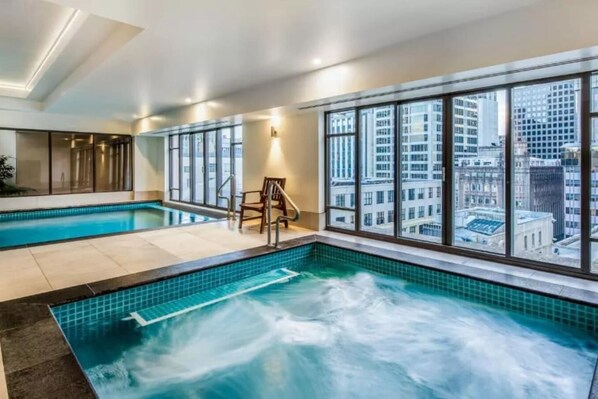 A hotel room with a large window, a pool, and a view of the city.