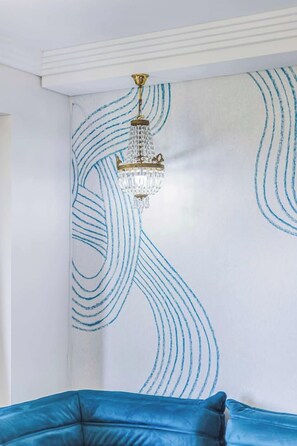 A room with a blue upholstered headboard, a wall with a blue abstract design, and a chandelier.