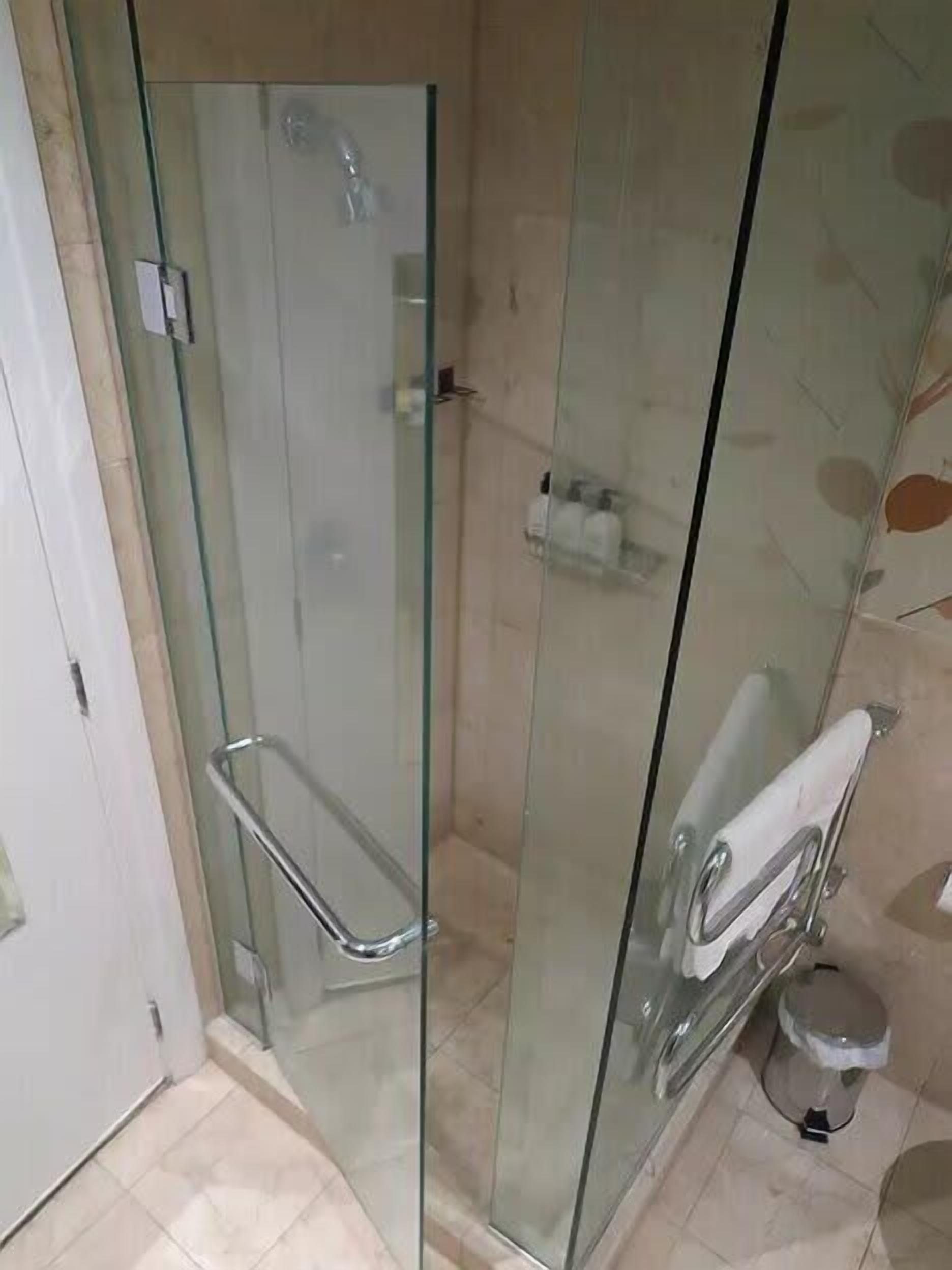 A glass-enclosed shower stall with a glass door, a glass shower enclosure, and a white towel hanging on the door.
