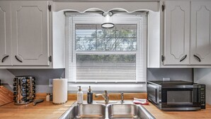 A kitchen with a double sink, a microwave, and a window with blinds. - Tranquil 2BR Apt Mpls - 8075 Apt 4 (Minneapolis)