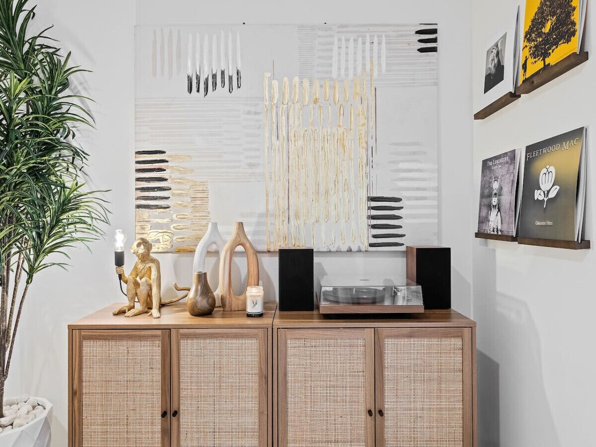Ein Zimmer mit einem Holzschrank, einer Pflanze und einer Wand mit abstrakter Kunst und gerahmten Bildern.
