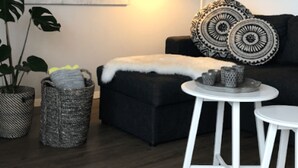 Una sala moderna con un sofá oscuro, una mesa de centro redonda, una lámpara blanca y un adorno de pared.