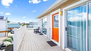 Une terrasse en bois avec une balustrade blanche, une porte orange vif et une porte vitrée donnant sur un espace abrité.