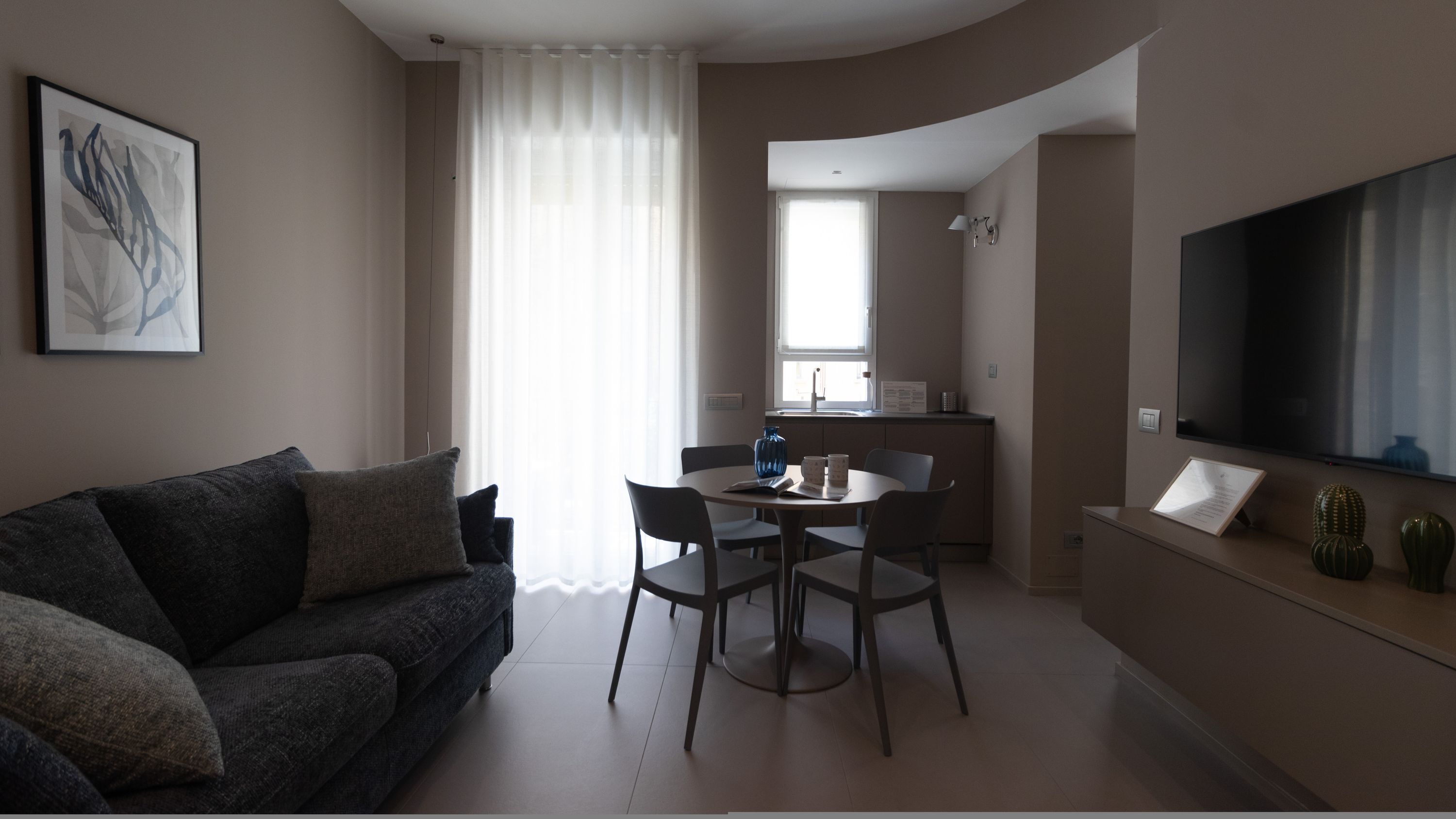 Un salon moderne comprenant un canapé, une table à manger avec des chaises, un coin cuisine et un téléviseur à écran plat fixé au mur.