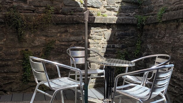 A patio with a table and chairs under a large umbrella, set against a stone wall.